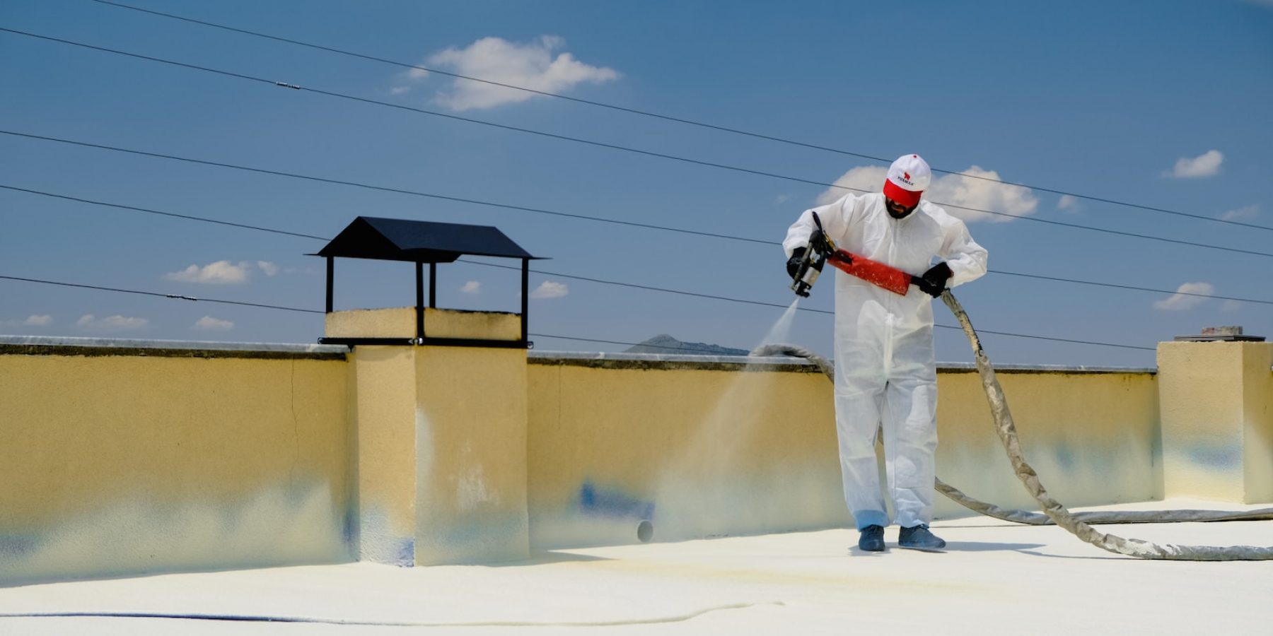 a man in a white coverall spray painting a roof